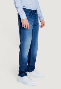 Jeans da uomo in denim blu con una leggera scoloritura, taglio dritto, cinque tasche e zip. Abbinati a sneakers bianche.
