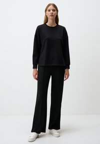 Felpa nera con una vestibilità rilassata e maniche lunghe, abbinata a pantaloni neri a gamba larga. Le sneaker bianche completano l'outfit.