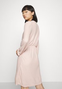 Vestido rosa claro, até ao joelho, com um padrão texturizado, corte descontraído, cintura elástica e mangas longas e largas.