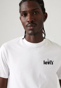 Weißes Baumwoll-T-Shirt mit schwarzem Levi's-Logo auf der Brust. Rundhals-Ausschnitt, kurze Ärmel und glatte Textur.