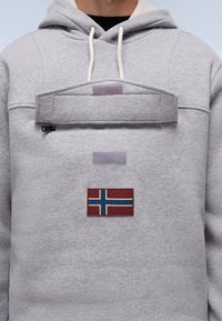 Grå hættetrøje med en frontlomme, der har en lynlås og en rektangulær klap. Inkluderer et syet patch af Norges flag. Blød stoftekstur.