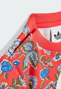 Mikina s kvetinovým vzorom na jasne červenom podklade, s modrými a zelenými akcentmi, rebrovaným výstrihom a jemnou textúrou látky.