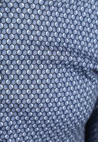 Blau-weißer Stoff mit einem hexagonalen Muster. Das Material wirkt glatt mit einem leichten Glanz und filigranen geometrischen Details.