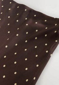 Hnědá látka s hladkou texturou a vzorem rovnoměrně rozmístěných krémových puntíků, mírně splývající.