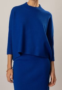 Pull en maille bleue oversize avec manches côtelées, col rond et texture douce, assorti à une jupe ajustée assortie.