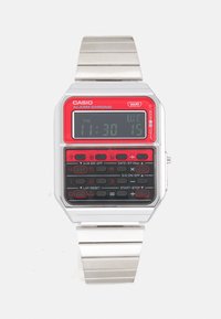 Relógio digital Casio com pulseira metálica prateada, mostrador retangular em vermelho e preto, e vários botões para funções como alarme e cronômetro.
