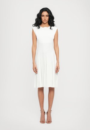 Witte geplooide jurk met een aansluitende bustier en korte mouwen, met horizontale strepen en een knie-lange zoom. Gemaakt met naakte strappy hakken.
