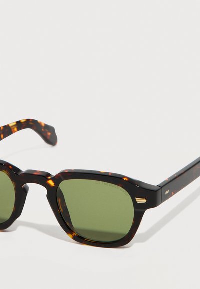 Ορθογώνια γυαλιά ηλίου με σχέδιο κελύφους χελώνας, πράσινους φακούς και χρυσές λεπτομέρειες στις άκρες του σκελετού και τα μπράτσα.