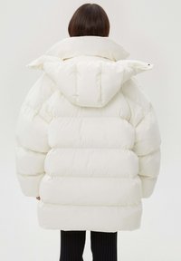 Biała pikowana kurtka puchowa z wysokim kołnierzem i dużym kapturem, o pikowanej teksturze i luźnym kroju, sięgająca poniżej bioder.