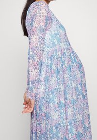 Sukienka w kwiaty z długimi rękawami o płynnej formie, w kolorach niebieskim, różowym i zielonym, wykonana z miękkiego, lekkiego materiału.