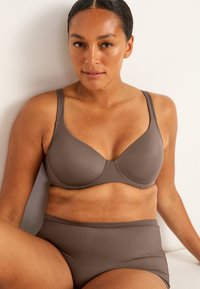 Brun trådlös bh och högmidjade trosor, tillverkade av slät tyg med en sömlös design. Har justerbara band och subtila sömnadsdetaljer.