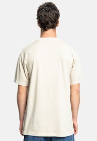 Béžové bavlněné tričko s krátkými rukávy, uvolněný střih a kulatým výstřihem, s hladkou texturou a minimálním švem na zádech.