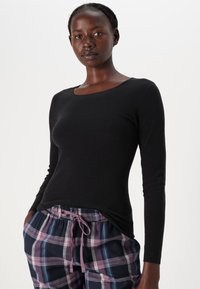 Haut à manches longues noir avec un col rond, associé à un pantalon de pyjama à motifs avec des carreaux en tons de bleu, violet et gris, doté d'un cordon de serrage.