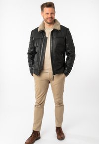 Zwart leren jasje met een beige nepbont kraag, rits aan de voorkant en twee zijzakken. Draagt over een lichte trui en gecombineerd met beige broek.