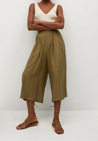 Olive’owe zielone spodnie szerokie z plisami, zestawione z dopasowanym kremowym topem w prążki. Modelka nosi beżowe sandały na rzemyki.