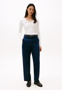 White long-sleeve top with three gold buttons and navy wide-leg trousers, complemented by a black belt and black loafers.