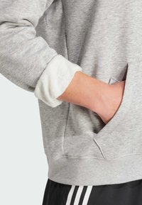 Grå sweatshirt med en texturerad tyg, med en vit fluffig mudd och en sidoficka. Designen inkluderar en avslappnad passform och en slät finish.
