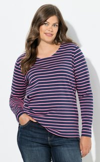 Navy ja vaaleanpunaisia raitoja sisältävä pitkähihaista paita, jossa on pyöreä kaula-aukko, pehmeä rakenne ja hyvin istuvat hihat, yhdistettynä tummansinisiin farkkuihin.