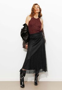 Haut dos nu métallisé bordeaux associé à une jupe longue en dentelle noire et des bottines noires ajustées. La jupe est ornée d'un ourlet en dentelle transparente en bas.