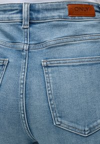 Φωτεινό μπλε τζιν από denim σε κοντινή λήψη που δείχνει τις πίσω τσέπες και ένα καφέ δερμάτινο λογότυπο με την ένδειξη "ONLY" στη μέση.