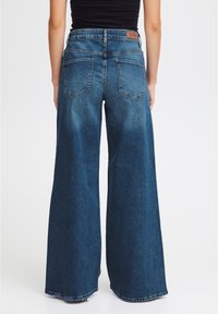 Jeans a gamba larga in denim blu scuro, con vita alta, tasche posteriori e un'etichetta in pelle con "ICH" in vita.