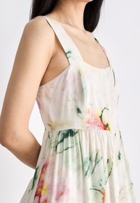 Robe à imprimé floral présentant des couleurs pastel, des bretelles larges, un décolleté carré et une taille froncée avec une jupe fluide.
