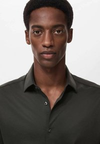 Camisa abotonada verde oscuro con cuello clásico, con una textura suave y un brillo sutil, colocada sobre un fondo neutro.