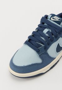 Blå og lyseblå sneakers med overdel i stof og læder, rund tå, polstret tunge, teksturerede snørebånd og en hvid gummisål.