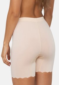 Beige shapewear korte broek met een gladde textuur, gegolfde zoom en een comfortabele tailleband, met een uitsparing voor functionaliteit.