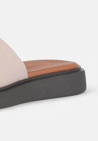 Beige leather sandal featuring a wide strap, brown insole, and black textured platform sole. Focus on minimalist design and clean lines.