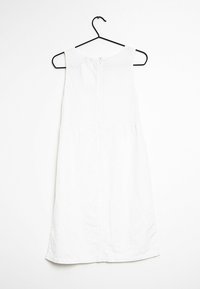 Witte mouwloze jurk aan een hanger, gemaakt van een lichtgewicht stof. Heeft een ritssluiting aan de achterkant en een licht uitlopende zoom.