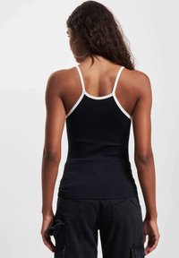 Top sportivo nero a coste con spalline sottili bianche, design aderente e superficie testurizzata. Indossato con pantaloni cargo neri. Vista posteriore mostrata.