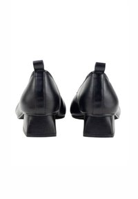 Zapatos negros de cuero con tacón bloque, con un lazo en la parte trasera y un acabado suave; cuentan con una punta redonda y un tacón robusto para mayor estabilidad.