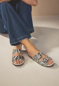 Sandal med zebra-mønster og to justerbare spænder, lavet af syntetisk materiale. Blød fodseng, open-toe design og struktureret sål.