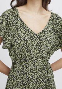 Svart blommig klänning med gröna och vita mönster. Har en V-ringning och volangärmar, tillverkad av lättviktsmaterial med knytning i midjan.