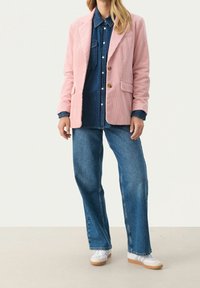Rosa corduroy-blazer med knappar och framfickor, lager på lager över en denimskjorta. Matchat med vida blå jeans och vita sneakers.