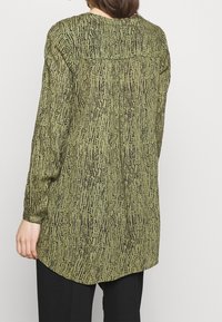 Langsleeve shirt in olijfgroen stof met een zwart abstract patroon, ronde zoom en subtiele plooidetail aan de achterkant.
