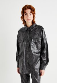 Schwarzes Kunstlederhemd mit Schlangenprint-Muster, mit spitzem Kragen, langen Ärmeln und zwei Brusttaschen mit Druckknöpfen.