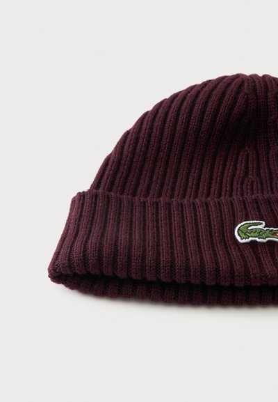 Bonnet en maille côtelée rouge foncé avec un revers et un petit écusson vert représentant un logo crocodile à l'avant.