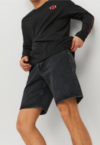 Musta pitkähihainen paita, jossa on punaisia grafiikoita, yhdistetty tummanharmaisiin farkkushortseihin, joissa on rento istuvuus ja näkyvät ompelusyöt.