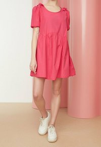 Roze katoenen jurk met korte mouwen,Gathered taille, strikaccenten op de schouders en een uitlopende rok; gecombineerd met witte sneakers.