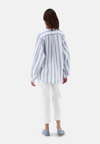 Camicia di lino a strisce blu chiaro e bianche con vestibilità ampia, maniche lunghe e piega sul retro, abbinata a pantaloni bianchi a vita corta e ballerine blu.