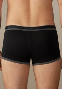 Schwarze Boxershorts aus weichem Material, mit einem grauen Bund mit Branding und einem enganliegenden Design, das die Form betont.