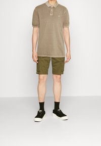 Beige poloshirt met een kraag, gecombineerd met olijfgroene cargoshorts met zijzakken en zwarte sneakers met witte zolen.