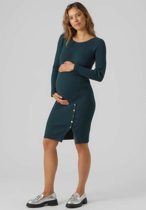Vestido de maternidad de tela acanalada en verde azulado oscuro. Presenta mangas largas, una silueta ajustada, un dobladillo a la altura de la rodilla y botones decorativos en el lateral.