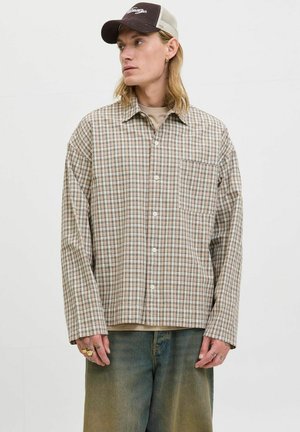 Brown and beige plaid shirt with long sleeves, button closure, and chest pocket. Worn over a light-colored shirt; paired with relaxed-fit jeans.