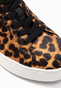 Sneaker con stampa leopardata realizzata in pelliccia sintetica, con lacci neri, punta tonda e suola in gomma bianca. La superficie testurizzata mette in risalto il motivo.