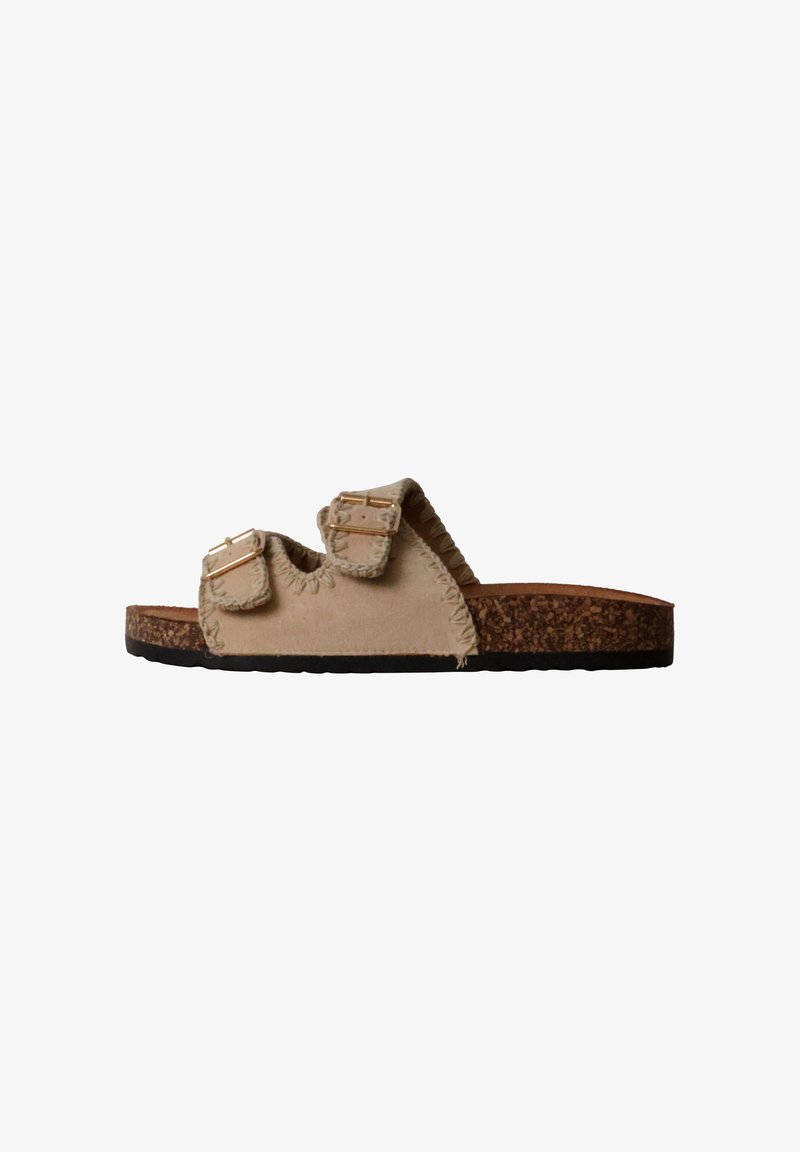 Sandale beige avec deux brides à boucle réglables, coutures apparentes et semelle à texture liège, présentée en profil latéral sur fond blanc.