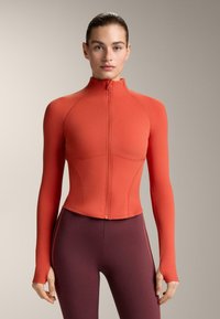 Rood sportjack met ritssluiting, lange mouwen, aangesloten pasvorm en een hoge kraag. Het materiaal lijkt glad met subtiele naaddetails.