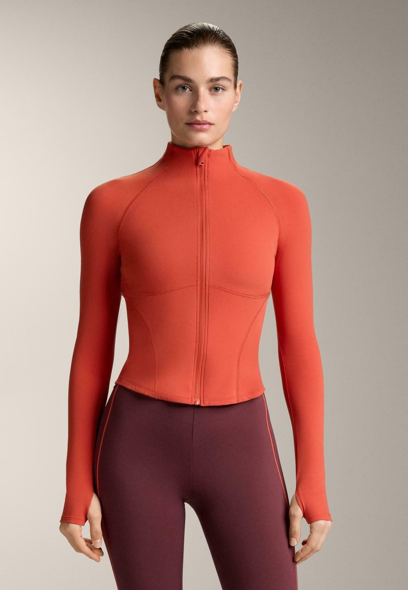 Rood sportjack met ritssluiting, lange mouwen, aangesloten pasvorm en een hoge kraag. Het materiaal lijkt glad met subtiele naaddetails.